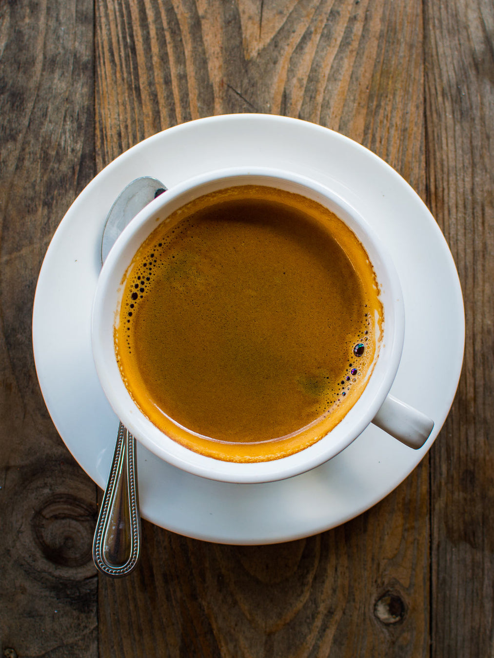 An image of a cup of coffee on a saucer with a teaspoon on the side